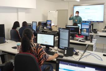 Turma em sala de aula com tela e computadores 