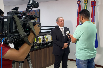 Homem de terno escuro, cabelos brancos, falando com homem forte de camisa verde