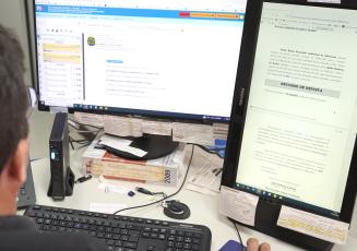 Dois monitores, um teclado e um homem de costa à esquerda.
