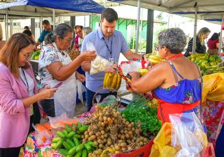 Quatro pessoas numa feira de frutas. À esquerda, uma mulher de blazer rosa.