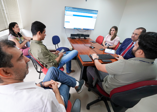 Grupo de pessoas, sendo duas mulheres e quatro homens, reunidos em frente a uma tela