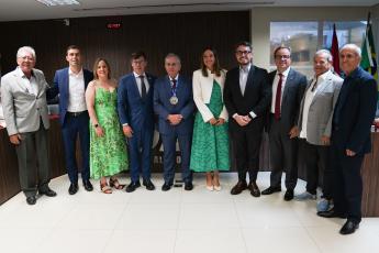 Homens e mulheres reunidos de pé para uma foto. Há dois homens de ternos na cor cinza claro  e seis de ternos escuros. As duas muleres estão de vestidos em tons de verde. Há um hoem usando uma medalha.