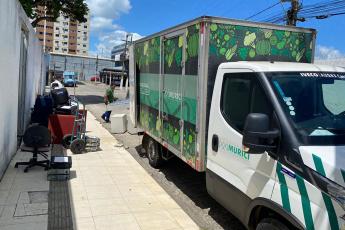 Caminhão barnco com baú verde, dois homens carregando uma estante para colocar dentro do caminhão
