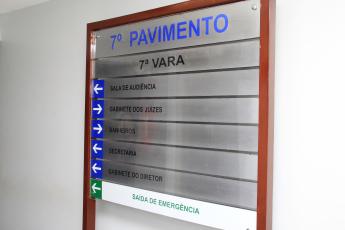 Painel indicativo de locais, em moldura de madeira com placas metalizadas. Há letras nas cores preta e azul. Em destaque tem escrito "7º pavimento"..
