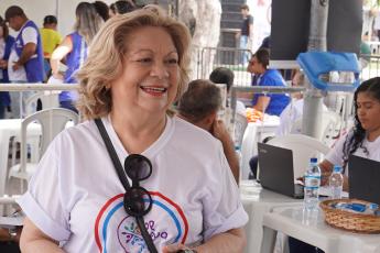 Mulher loira, de camisa branca cerca por pessoas fazendo atendimento público