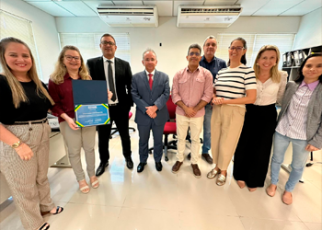 Grupo de pessoas em pé em um semi círculo, com uma das mulheres com um certificado na mão