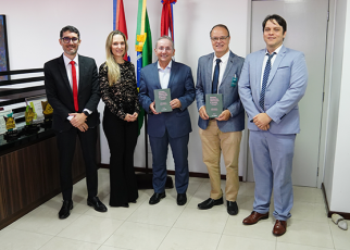 Foto de cinco pessoas de pé, sorridentes, um deles, o desembargador Marcelo Vieira, ao centro, segurando um livro