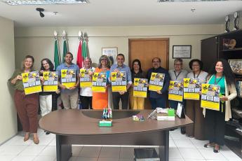 Grupo de homens e mulheres em trajes formais segurando um cartaz amarelo com o dizer Prêmio Trabalho Seguro