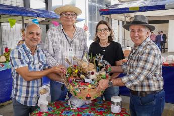 Três homens de camisa de xadrez e uma mulher de blusa preta segurando um balaio com produtos da feira agroecológica