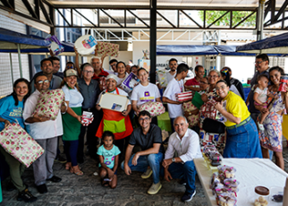 Há um grupo de pessoas posando para fotos. Uns estão de pé e outros agachados. Algumas dessa pessoas estão com presentes nas mãos.a