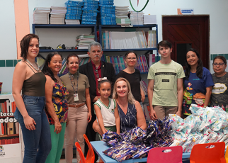 Várias pessoas reunidas para uma foto. Há embalagens em cima das mesas escolares infantis.
