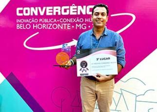Fundo rosa com letra branca escrito convergência e um homem branco com camisa jeans azul clara com um certificado na mão