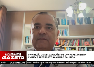 A imagem mostra um homem participando de uma entrevista por vídeo, com estante de livros ao fundo. Na parte inferior, há uma tarja com o título da matéria exibida no telejornal “Boletim Gazeta”: “Proibição de declarações de comparecimento em UPAs repercute no campo político”.