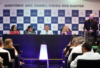 A imagem mostra uma mesa de autoridades durante o lançamento da Liga de Combate ao Assédio em Alagoas, realizado no auditório Adv. Carmil Vieira dos Santos, do Tribunal Regional do Trabalho da 19ª Região (TRT-19). Ao fundo, há um painel com o logotipo da Justiça do Trabalho e do TRT-19. No centro da imagem, uma placa iluminada com a frase “Quebre o silêncio” reforça o mote do evento, que tem como objetivo o enfrentamento ao assédio moral e sexual no ambiente de trabalho. O público acompanha atentamente.