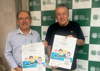 Dois homens idosos segurando um cartaz grande; um homem usa camisa social azul clara e o outro camiseta preta