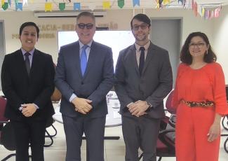 Três homens de terno escuro e uma mulher de roupa vermelha, todos em pé