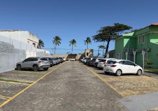 Há um estacionamento com alguns carros e uma casa verde ao lado