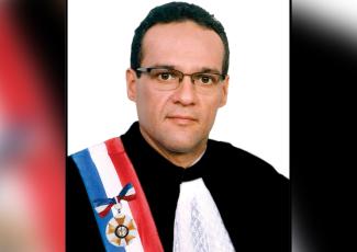 Há um homem vestido de toga com faixa de listras azul, branca e vermelha
