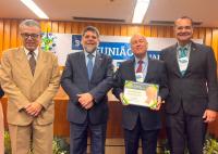 Há quatro homens de terno. Um deles segura um certificado.