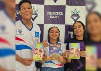 Há três adolescentes segurando um gibi. Sendo o primeiro um garoto com uniforme. E duas meninasde camisetas de malhas nas cores, branca e lilás.