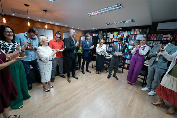 Vários homens e mulheres reunidos de pé em um círculo. Todos estão aplaudindo.