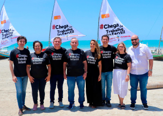 Grupo de homens e mulheres com camisas pretas com a frase "Chega de trabalho infantil", em frente às jangadas com as velas com a mesma frase