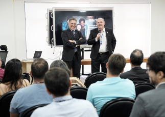 Dois homens de terno á frente de uma plateia