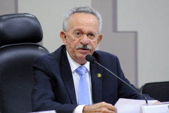 Homem idoso de cabelo grisalho, usando terno preto, camisa branca e gravata azul claro.