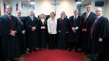 seis homens de toga preta e ao centro três mulheres, sendo duas de toga preta e uma de calça preta e camisa branca
