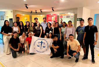 Várias pessoas reunidadas parauma foto. Umas estão de pé e há outras agachadas. Elas seguram uma bandeira com uma logomarca.
