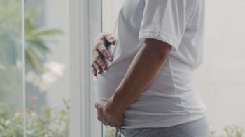 Perfil de mulher gestante segurando a barriga. Ela veste blusa branca e calça cinza.