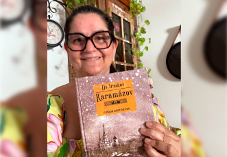 Mulher brande de cabelos pretos amarrados e óculos preto segurando um livro