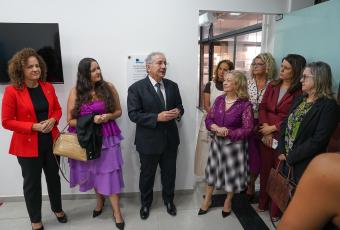 Várias pessoas em pé, sendo um homem de terno preto e diversas mulheres, todas usando rupas sociais