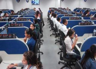 Foto com vários operadores de telemarketing, homens e mulheres, sentados trabalhando.