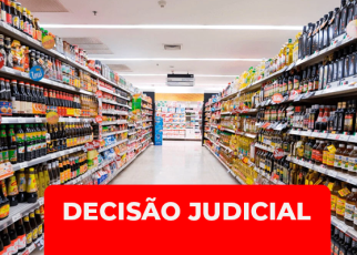 Imagem de um corredor de supermercado, com prateleiras cheias de produtos dos dois lados. Em destaque, na parte inferior da imagem, há uma faixa vermelha com o texto em branco: “DECISÃO JUDICIAL”.
