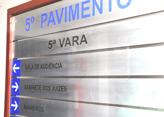 A imagem mostra uma placa de sinalização interna de um prédio. Nela está escrito em destaque “5º PAVIMENTO” e “5ª VARA”. Há também setas indicando direções para “SALA DE AUDIÊNCIA” e “GABINETE DOS JUÍZES”.