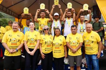 Grupo de pessoas vestidas de camisetas amarelas. O grupo da parte que tá mais elevada erguer troféus.