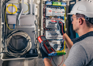 Homem trabalhando em quadro de energia. Ele utiliza esquipamentos de proteção.