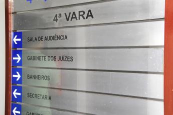 Placa de metal com moldura em madeira, há letras pretas escrito em destaque 4ª Vara.. Há setas indicativas.