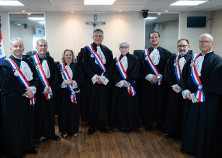 Oito pessoas sendo duas mulheres e seis homens, todos usando uma toga preta com a faixa branca, azul e vermelha cruzando o peito