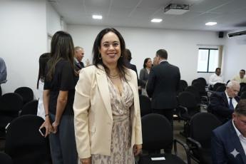 Mulher morena de cabelos pretos e roupa creme em pé e sorrindo para a foto