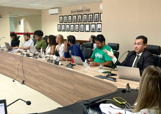 Várias pessoas, entre homens e mulheres, sentado em uma bancada participando de uma reunião