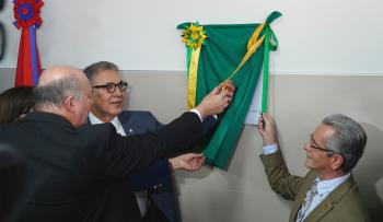 Foto de três homens de terno e gravata descerrando uma faixa verde e amarela