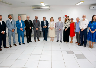 Foto de nove homens e quatro mulheres todos em pé. Todos os homens usam ternos e as mulheres, roupas sociais.