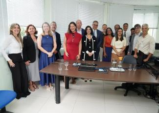 Foto de 25 pessoas em pé posadas para a foto, entre homens e mulheres. Homens usam ternos e mulheres vestidos e roupas foramais
