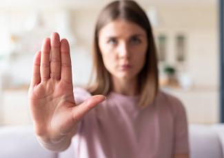 Há uma mulher de cabelos lisos com o braço estendido e mão estendida a frente, em situação de defesa
