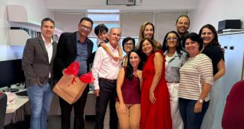 Grupo de pessoas posando para foto. Eles estão sorridentes. Há a penas uma criança. Ela está pendurado nas costa de um senhor.