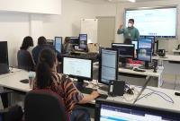 Turma em sala de aula com tela e computadores 