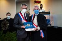 Ministro do TST Vantuil Abdala recebe das maõs do desembargador do TRT-19, Marcelo Vieira, a comenda da Ordem do Mérito. Os dois homens estão de pé, vestindo terno escuro e usando máscara