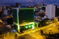 Em tfoto tirada do alto, prédio sede do TRT-19 com iluminação verde, em homenagem ao Abril Verde
